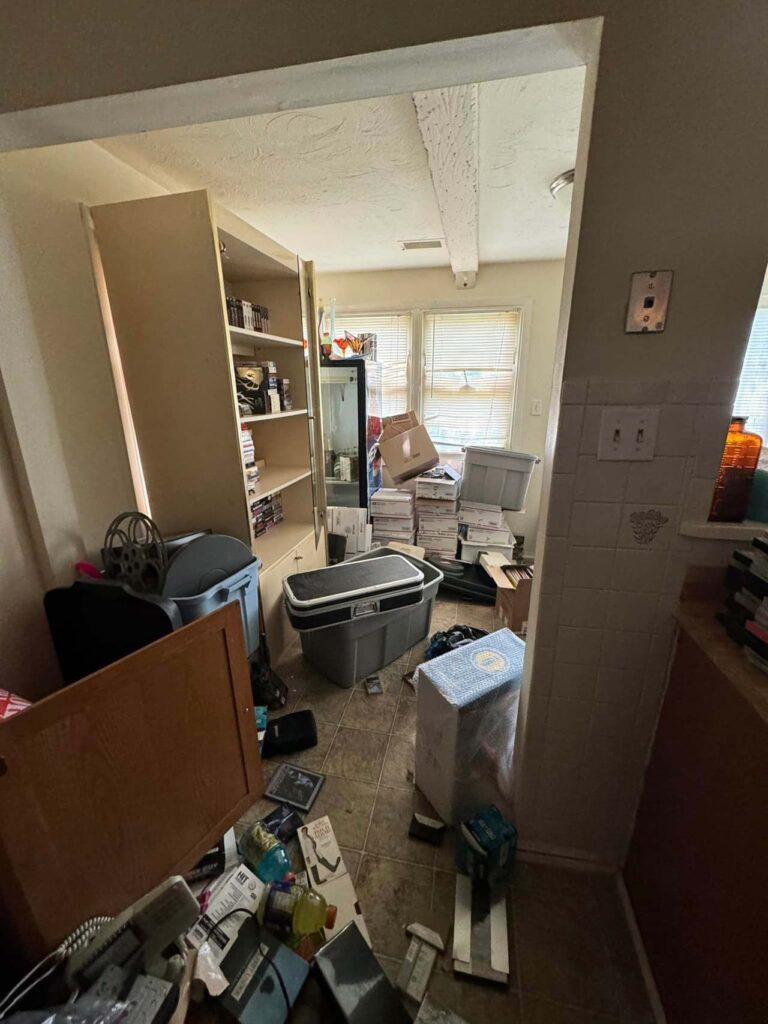 A cluttered kitchen filled with disorganized items and furniture, showcasing a chaotic and untidy environment.