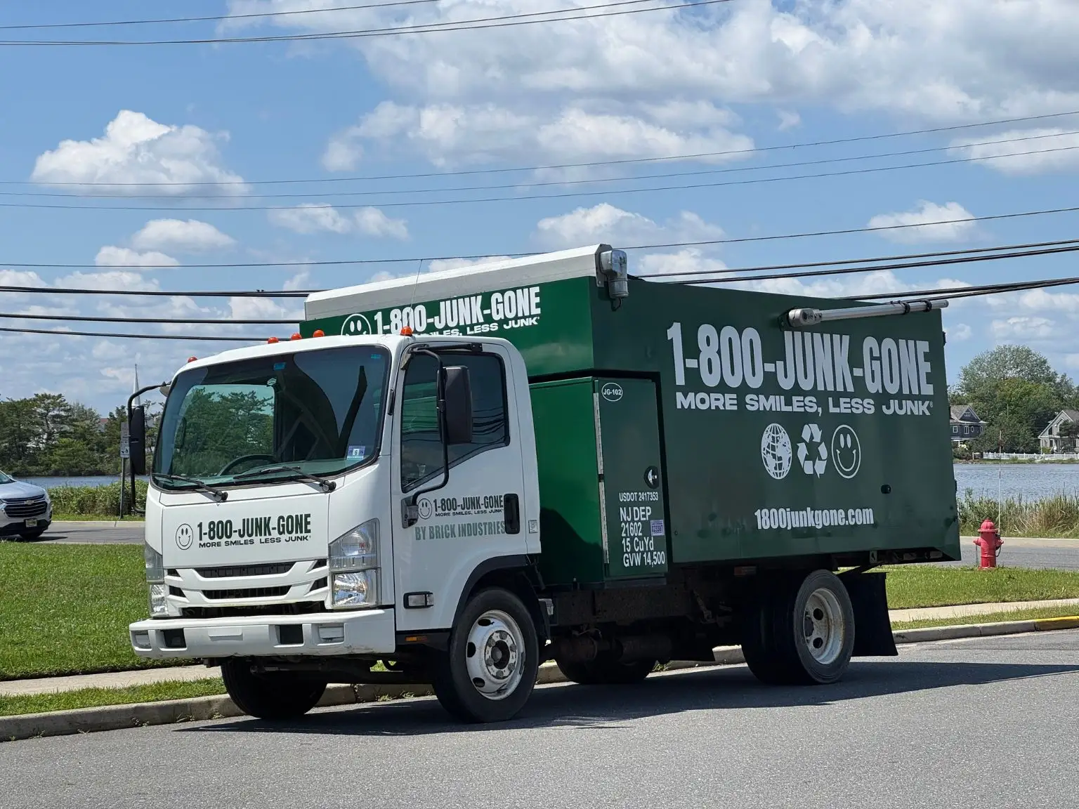 Side view of a green and white 1-800-JUNK-GONE removal truck parked along a suburban road