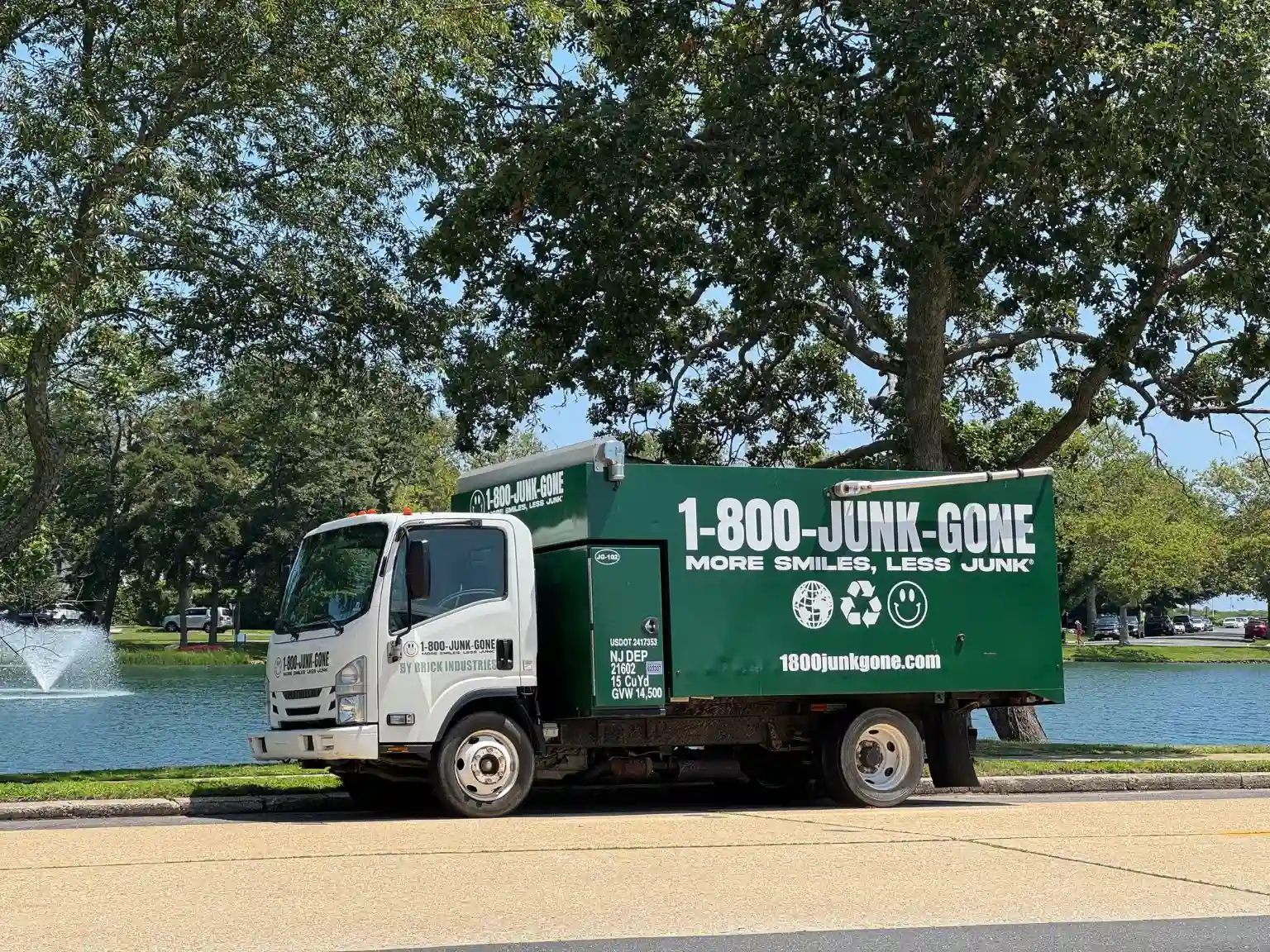 Side view of a green 1-800-JUNK-GONE truck parked near a lake with a fountain in the background