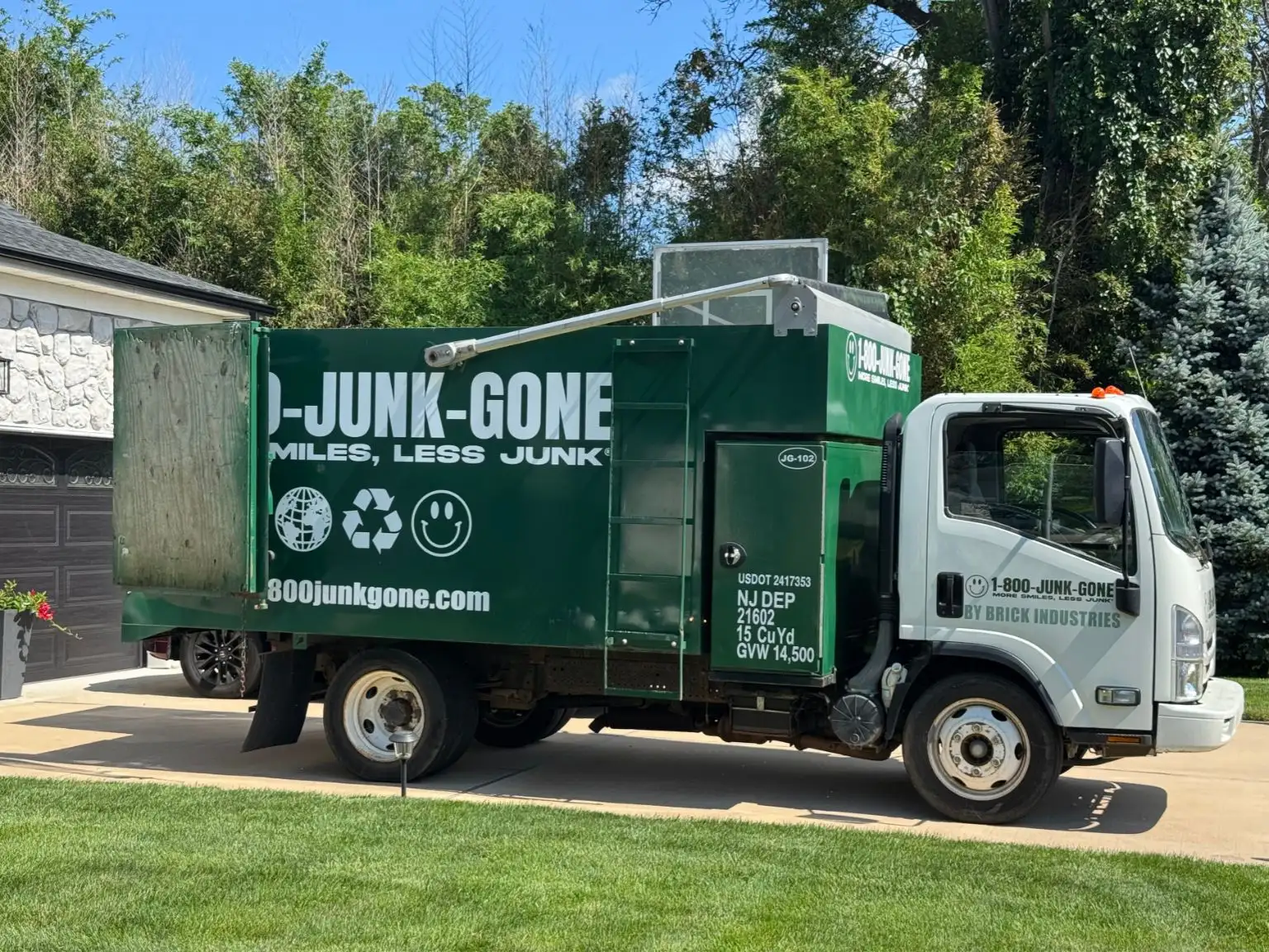 Full side profile of a green 1-800-JUNK-GONE removal truck parked in a residential driveway