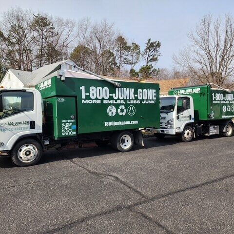 Two green 1-800-JUNK-GONE trucks parked on a residential street, ready for junk removal services.