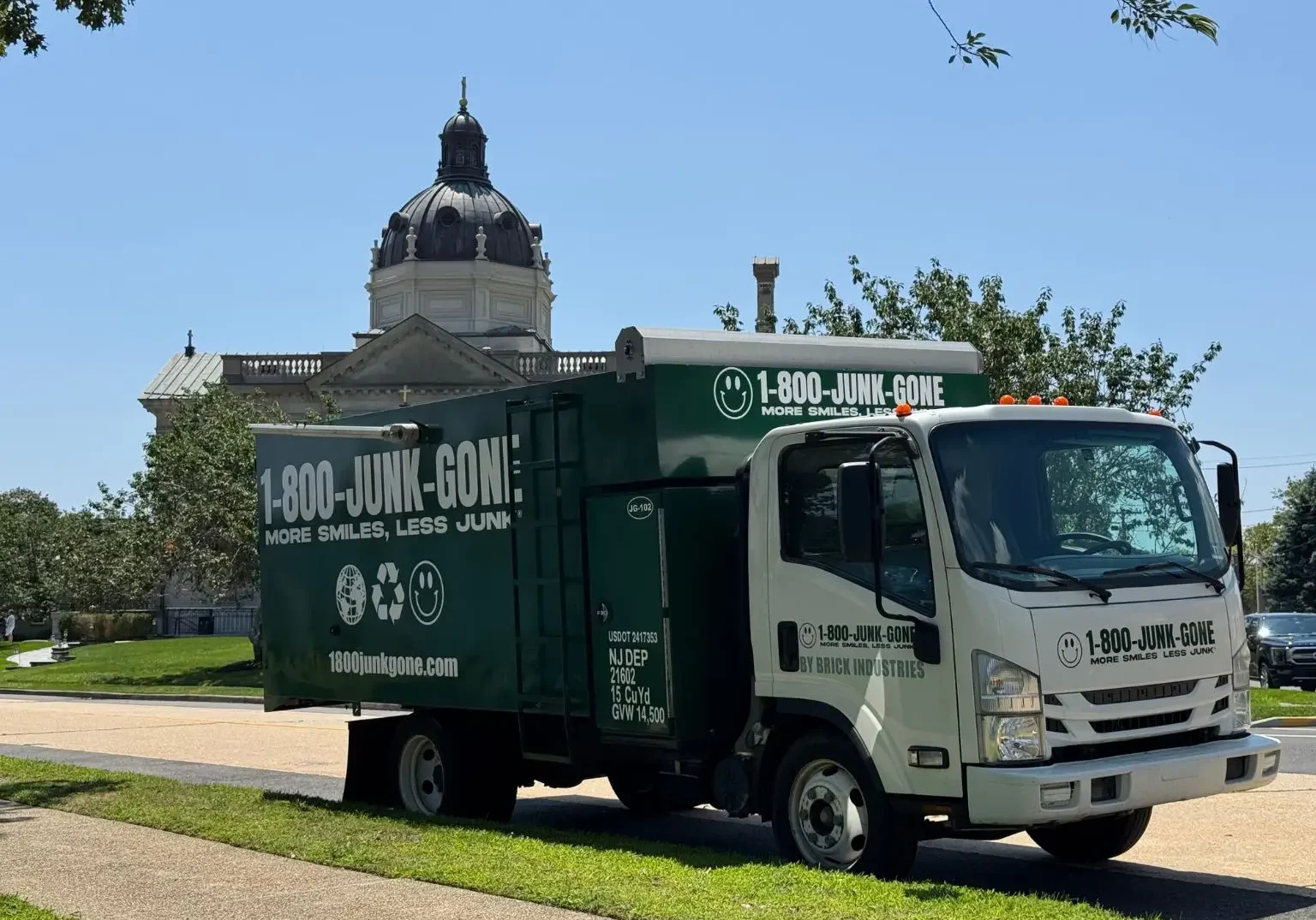 Three-quarter view of a white cab and green box 1-800-JUNK-GONE truck parked along a curb