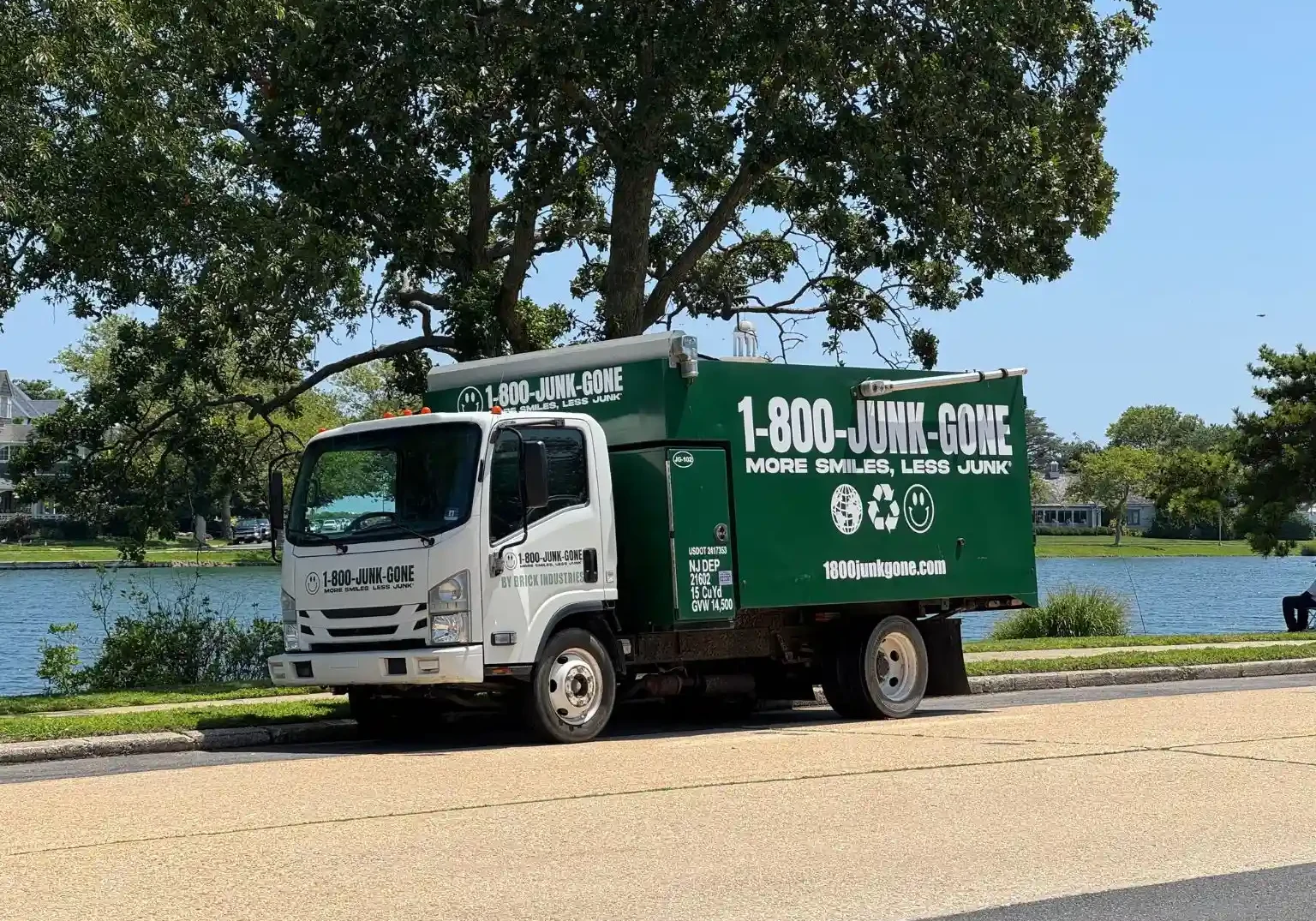 Side profile of a 1-800-JUNK-GONE truck parked along a scenic lake road under shade trees