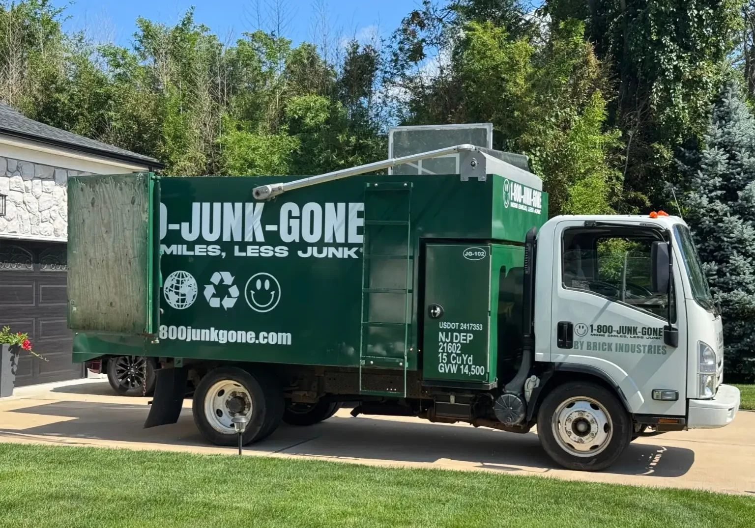 Full side profile of a green 1-800-JUNK-GONE removal truck parked in a residential driveway